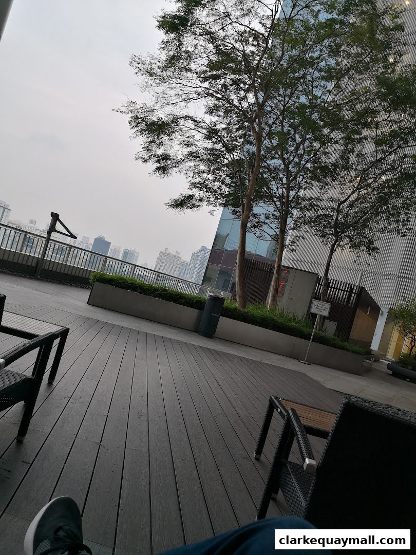 A person's legs are visible in the foreground on a wooden deck with chairs and trees.