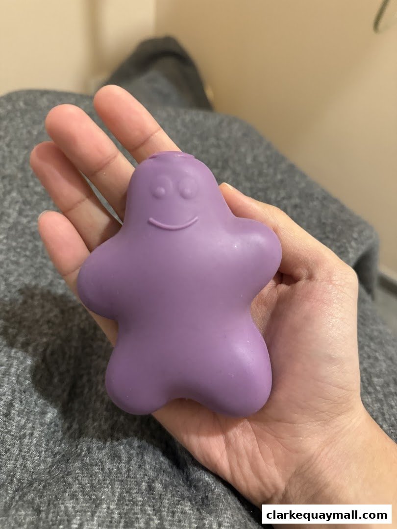 A hand holds a purple, star-shaped toy with a smiley face.