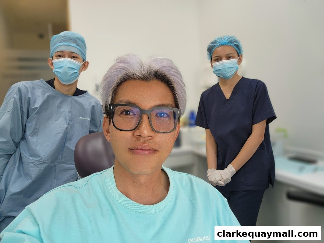 A person in a light blue shirt poses with two dental professionals in scrubs and masks.