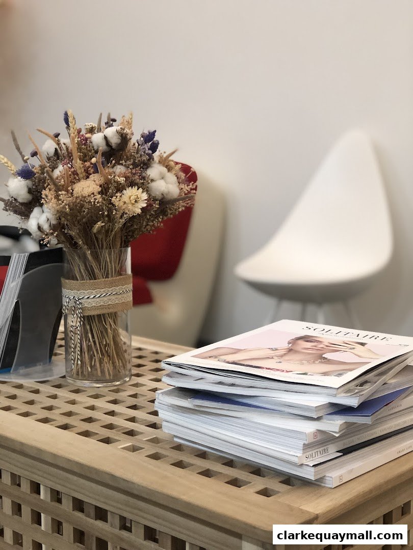 A stack of magazines and a vase of dried flowers on a wooden table.