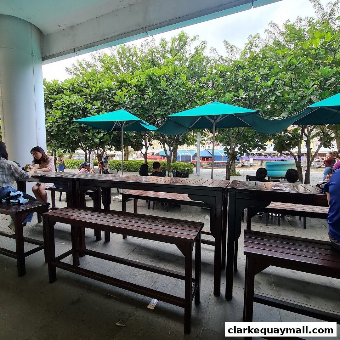People dining at outdoor tables with green umbrellas and trees in the background.