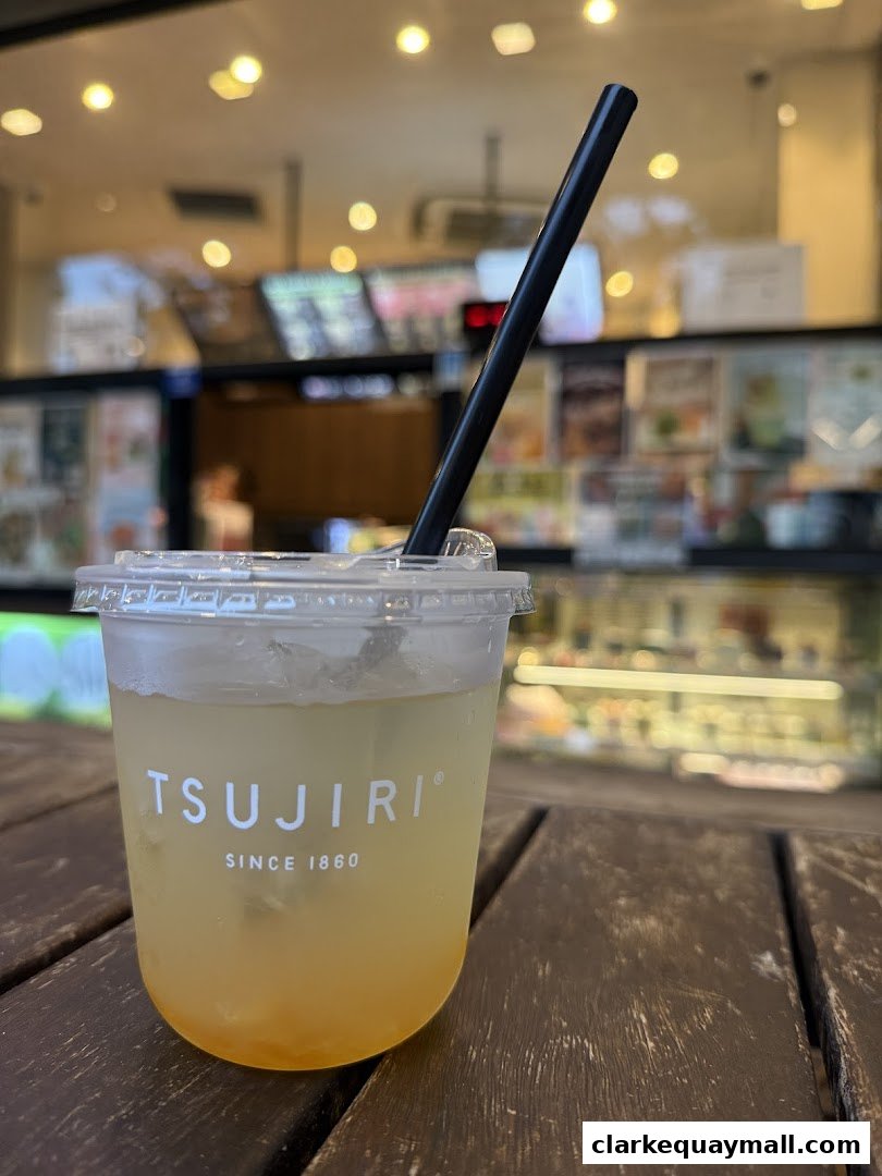 A refreshing iced beverage with a straw sits on a wooden table in front of a blurred shop interior.