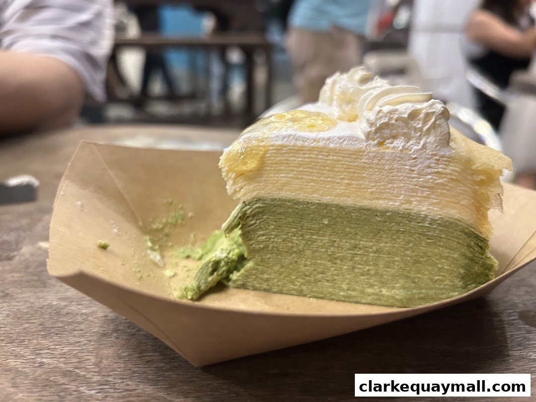 A slice of layered matcha and cream cake with whipped cream and syrup on top.