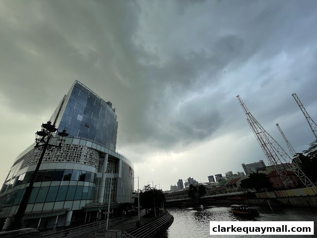 A modern glass building stands beside a river under a cloudy sky.