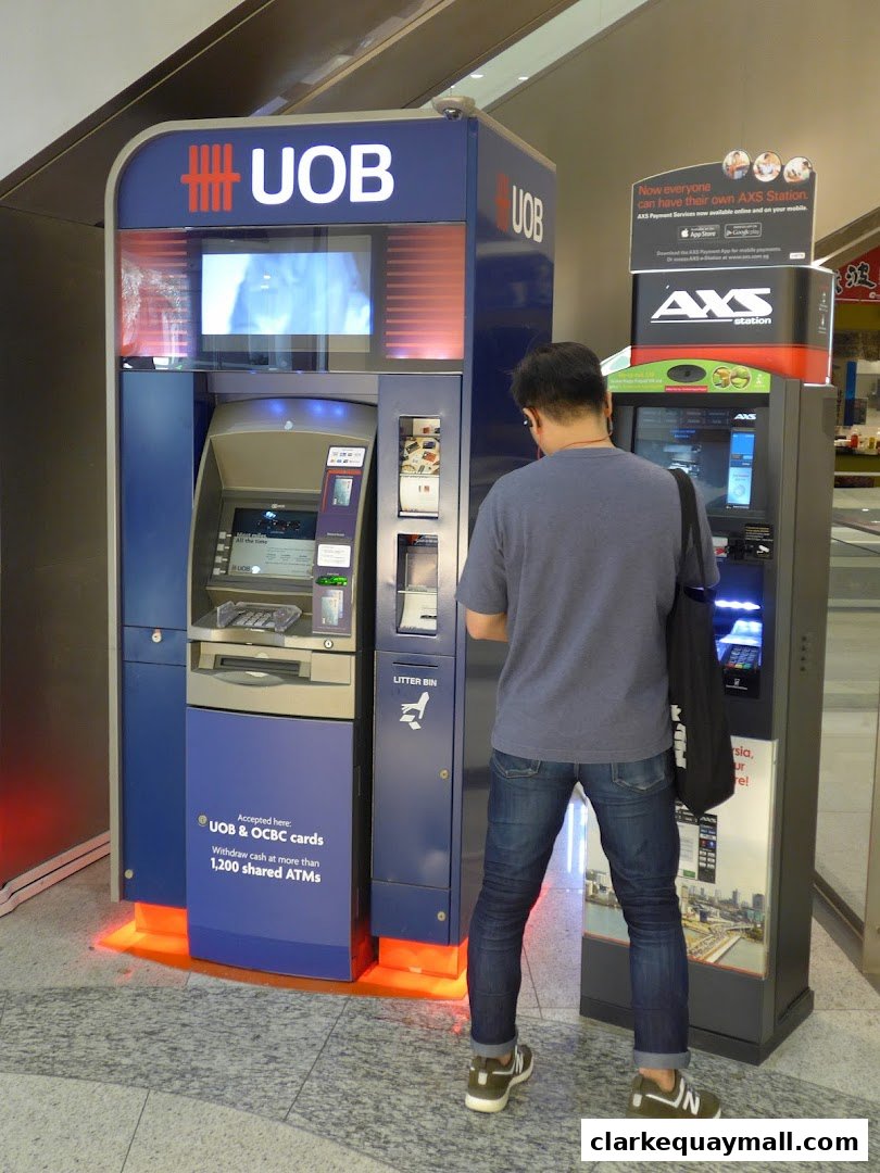 A man uses a UOB ATM machine next to an AXS station.