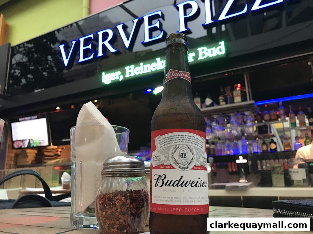A bottle of Budweiser beer sits on a table in front of the Verve Pizza Bar.