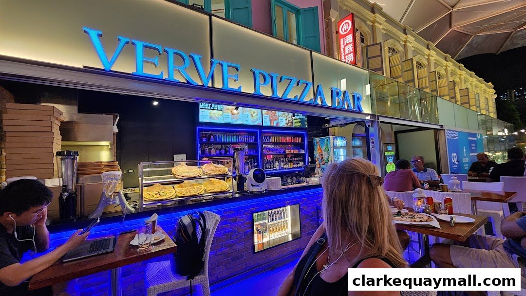 Verve Pizza Bar storefront with illuminated signage, display of pizzas, and customers dining outdoors.