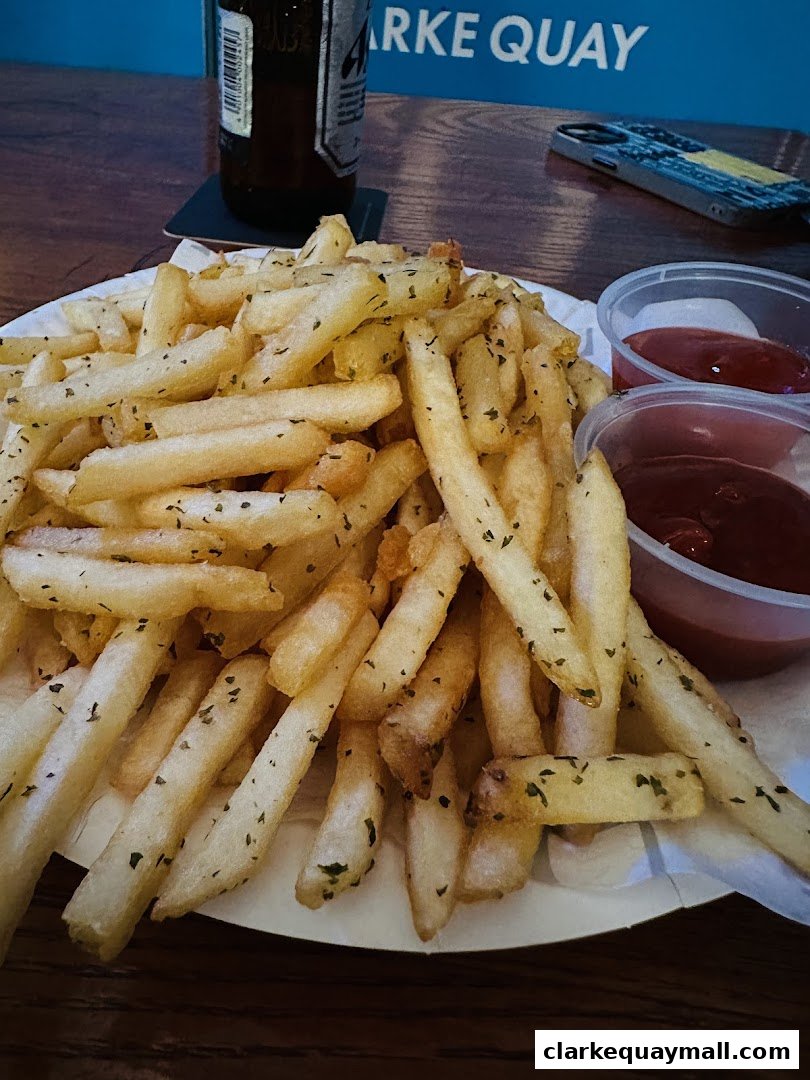 A plate of seasoned french fries with ketchup and a bottle of beer.