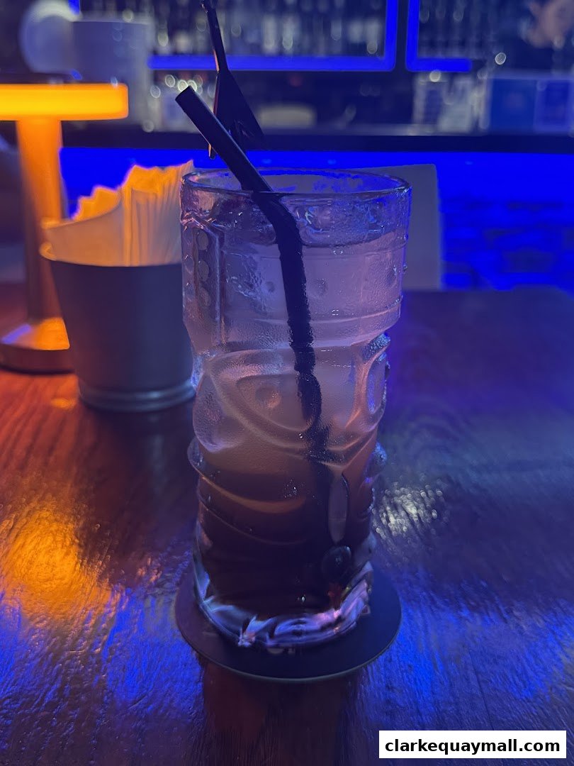 A tiki-style cocktail with straws sits on a wooden bar with blue and orange lighting.