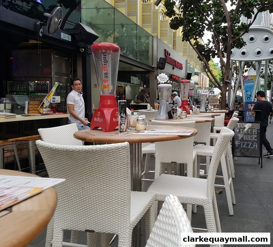 Outdoor seating area of a pizza bar with tables, chairs, and a beer dispenser.