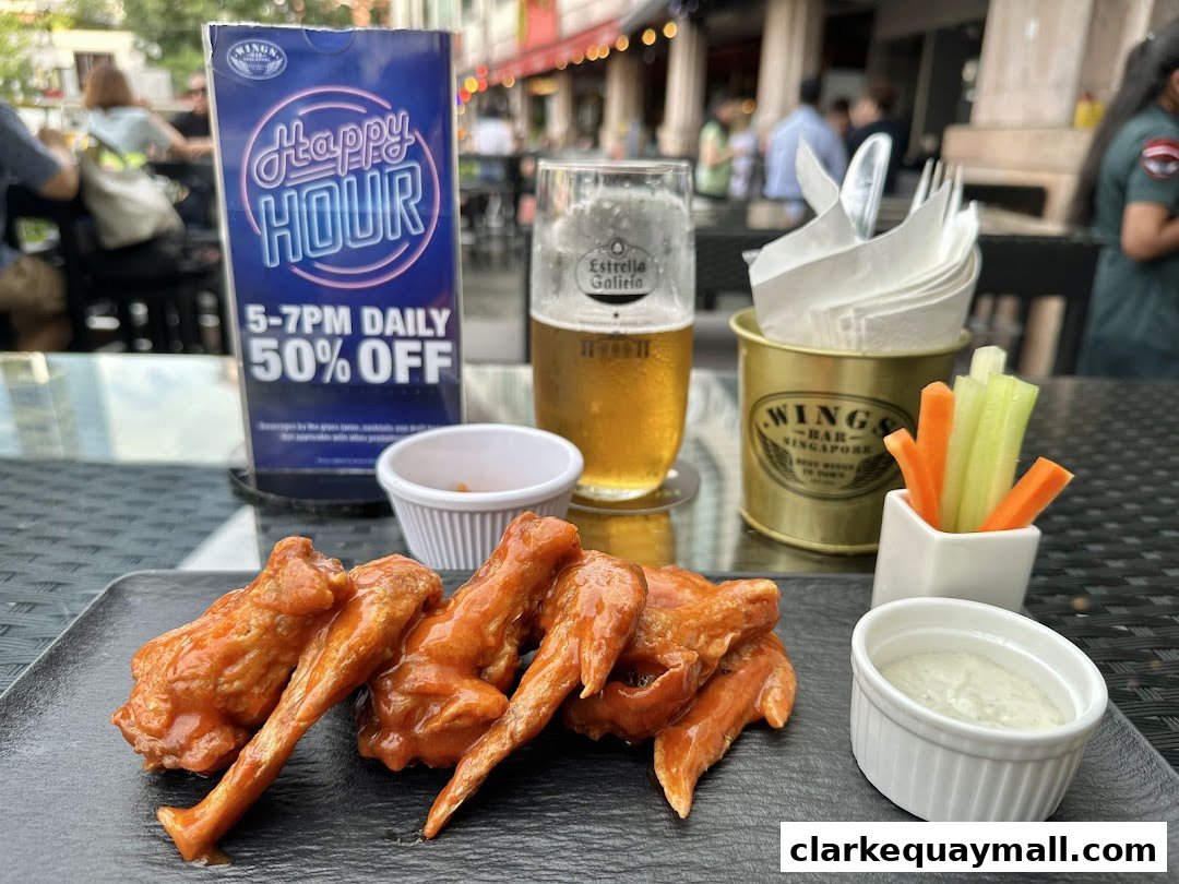 A plate of buffalo wings with a side of ranch dip, celery, and carrots, plus a beer.
