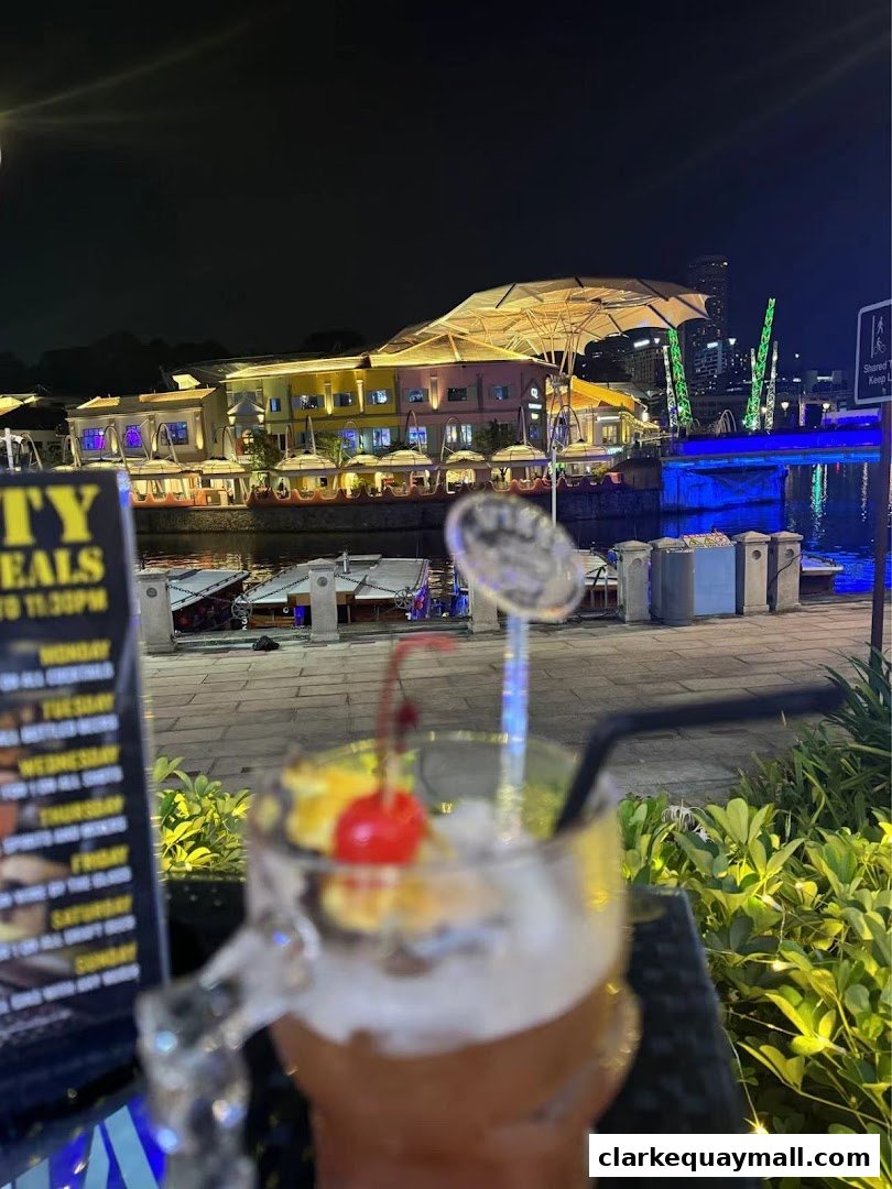 A cocktail with a cherry and whipped cream sits on a table with a menu and a waterfront view at night.