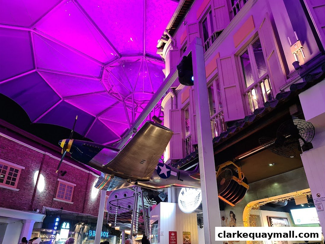 A vintage airplane suspended under a purple canopy, with a brick building and shuttered windows.