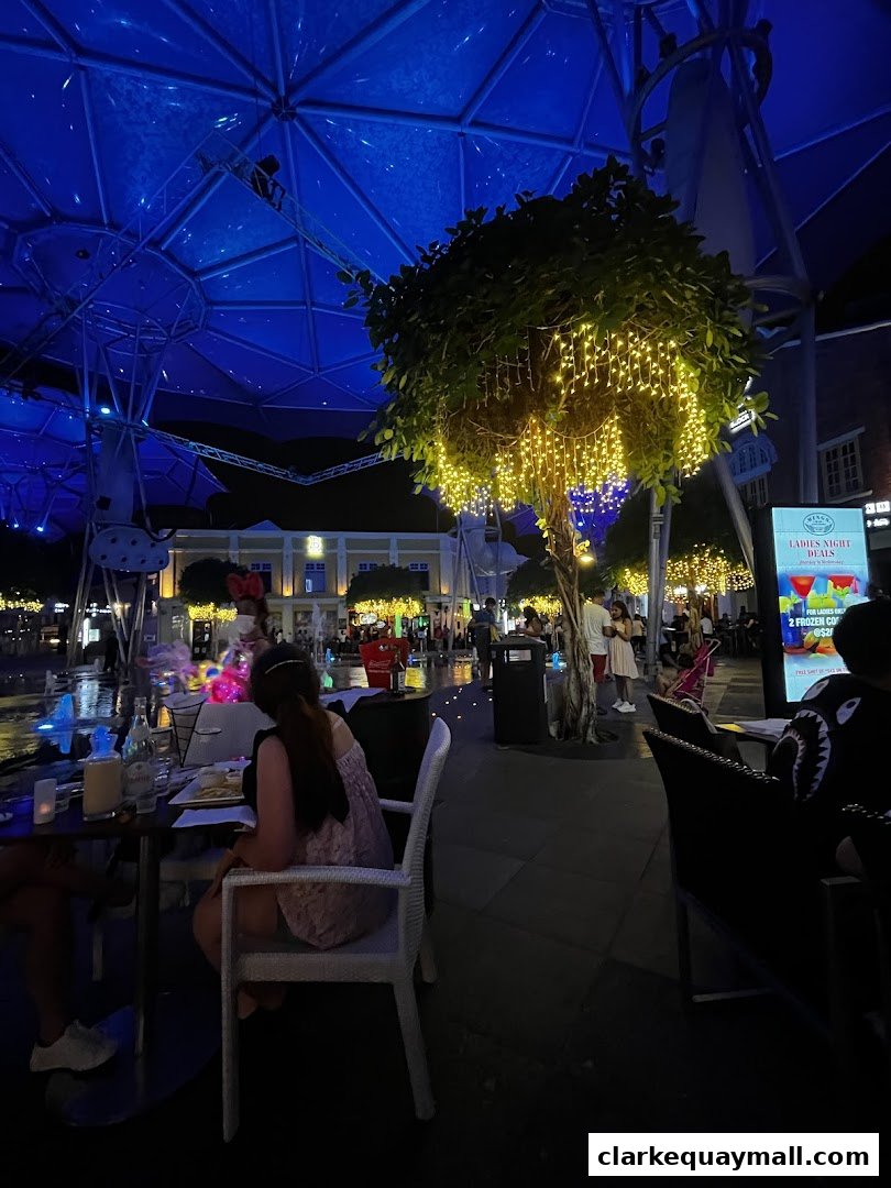 An outdoor dining area at night with people seated at tables under a blue illuminated canopy.