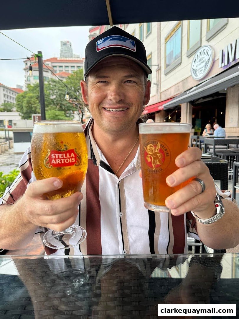 A man smiles holding two glasses of beer in front of a bar.