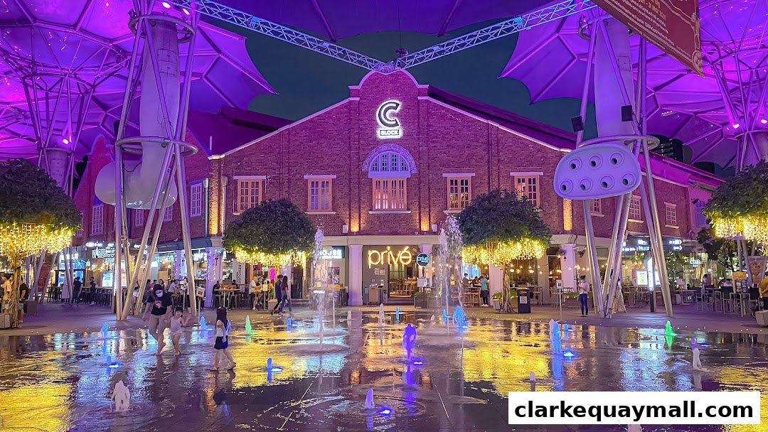 A lively evening scene with a fountain and illuminated buildings, featuring people enjoying the atmosphere.