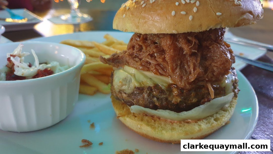 A close-up of a pulled pork burger with cheese and fries, served with a side of coleslaw.