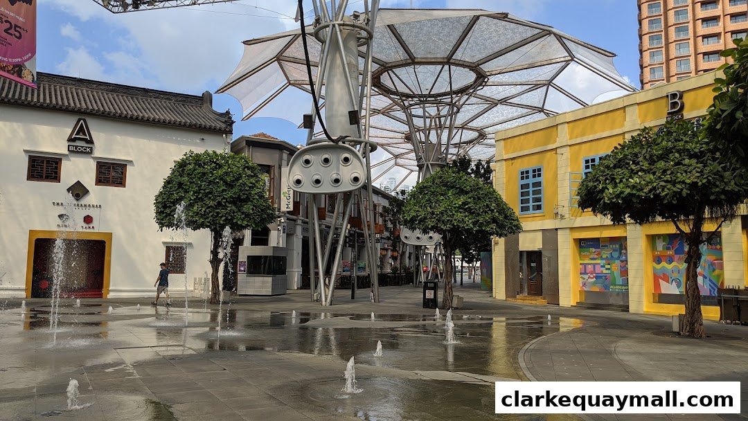 An outdoor plaza with fountains and shops, featuring a yellow building with blue windows and a white building with traditional architecture.