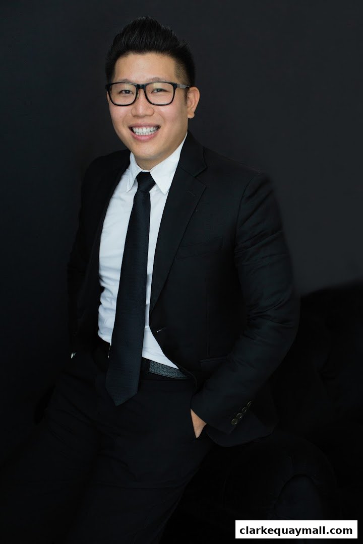 A professional portrait of a smiling man in a black suit and tie against a dark background.