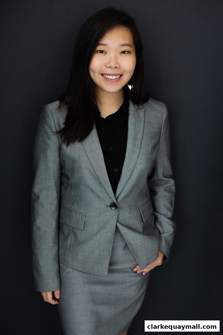 A professional portrait of a smiling woman in a grey suit against a dark background.