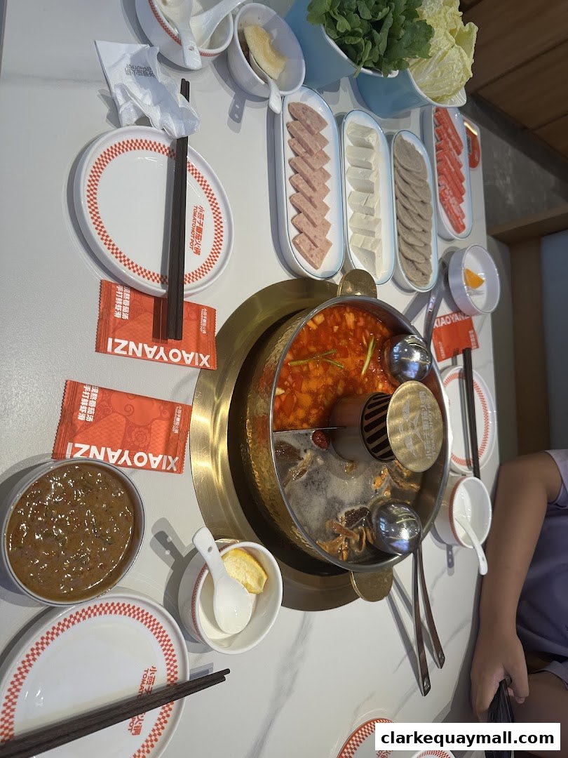 A table set for hot pot with various ingredients and a bubbling tomato broth.