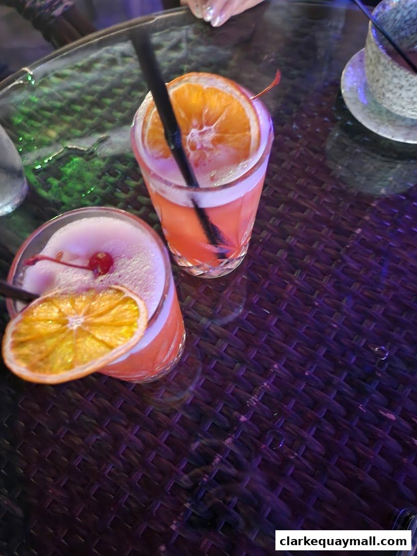 Two refreshing cocktails with orange slices and cherries on a table.