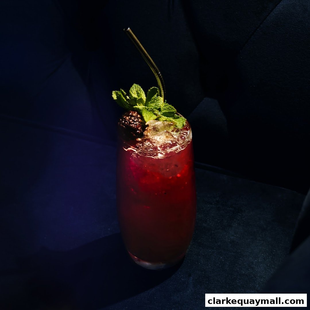 A tall glass of a dark red cocktail garnished with mint and a blackberry.