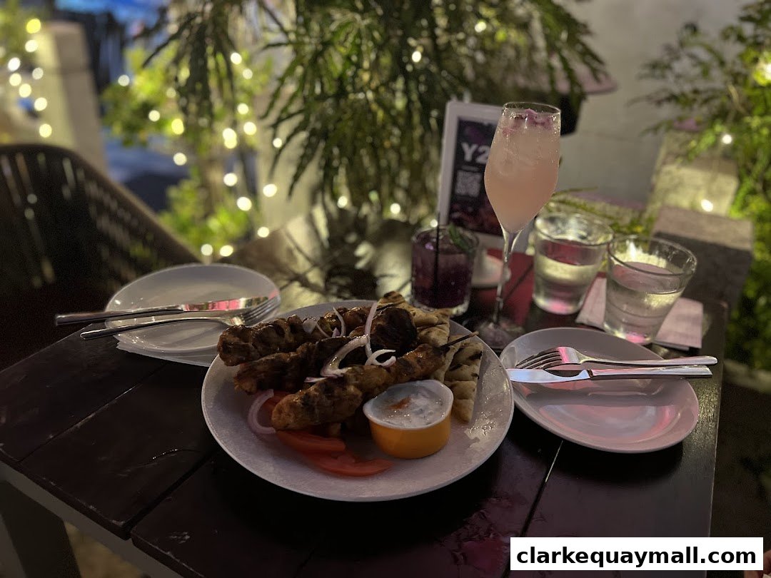 A plate of grilled meat skewers with pita bread and dip, served with drinks.