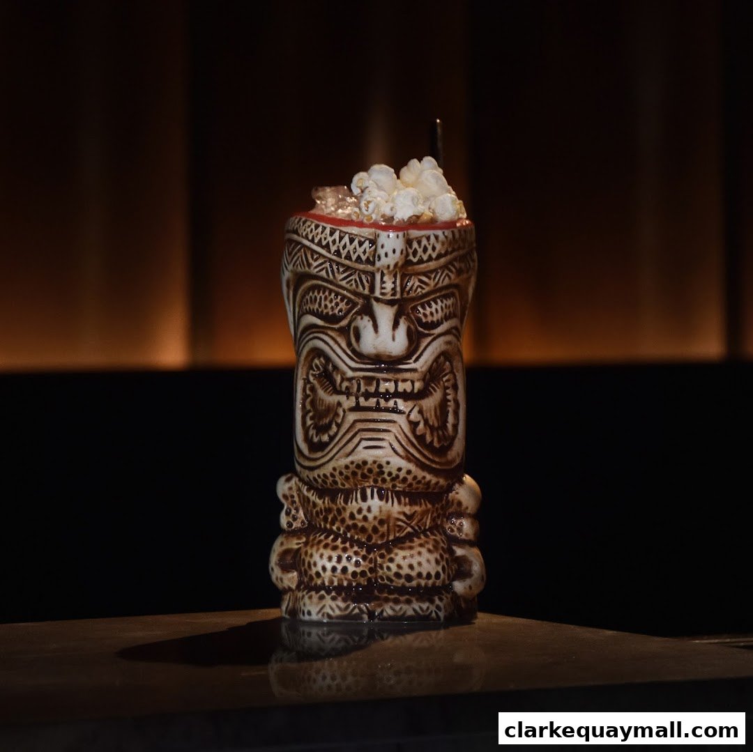 A tiki mug cocktail topped with popcorn and ice sits on a dark surface.
