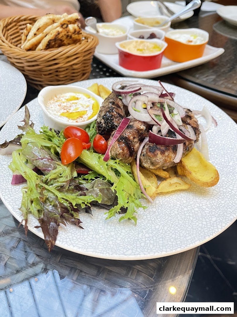 A plate of grilled meat with salad, fries, and dips, served with pita bread.