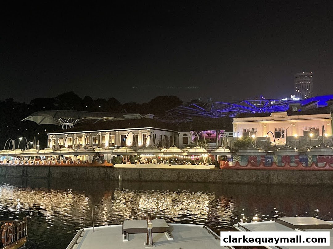 A lively riverside dining scene at night with illuminated buildings and reflections on the water.