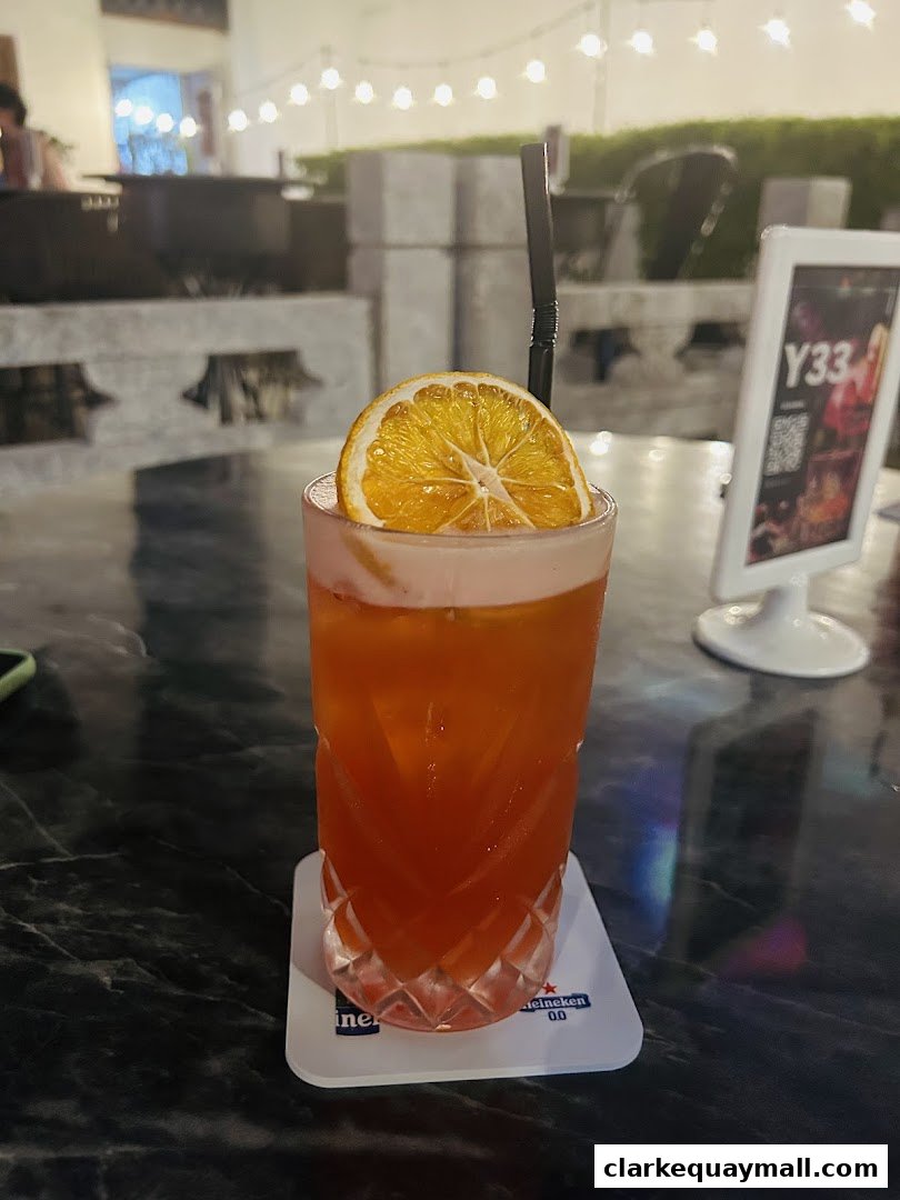 A refreshing cocktail with a slice of dried orange and a straw, served on a coaster.