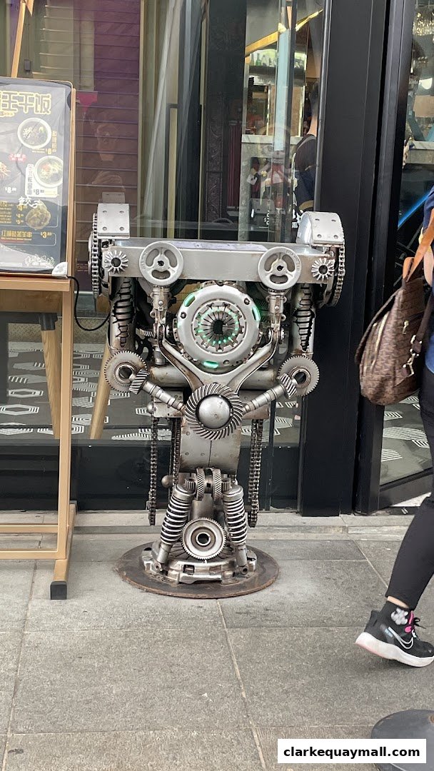 A unique metal robot sculpture is displayed outside a shop with a glass facade.