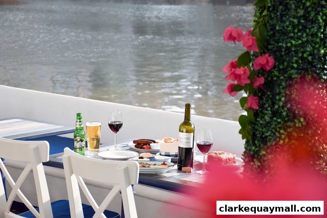 A table setting with food, drinks, and a bottle of wine by the water.
