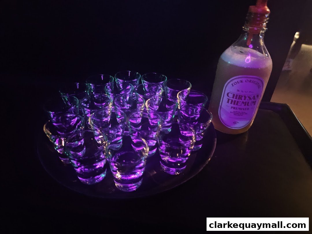 A tray of shot glasses illuminated with purple and green lights next to a bottle of premixed drink.