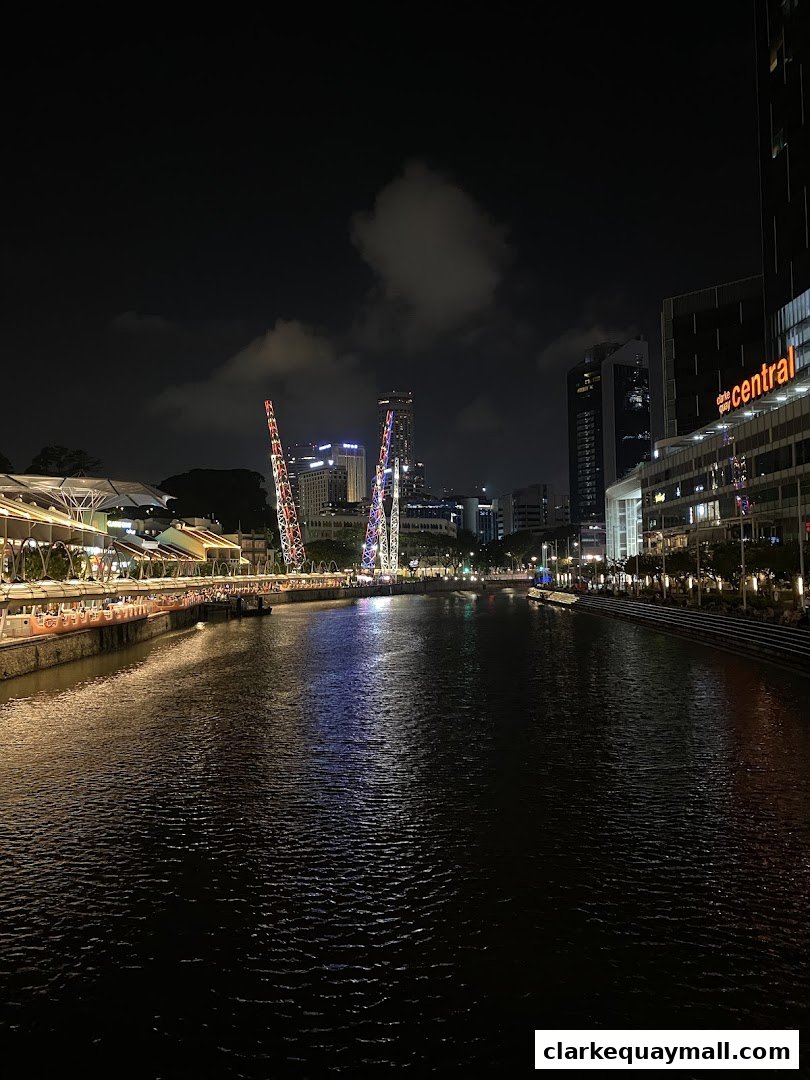 A nighttime view of a riverfront with illuminated buildings and a boat on the water.