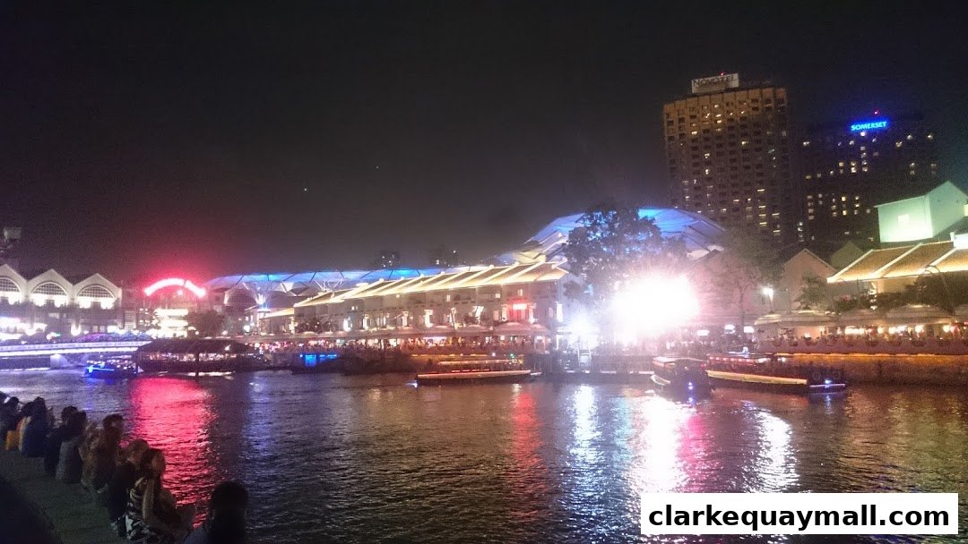 A vibrant nighttime view of a riverside promenade with illuminated buildings and boats.